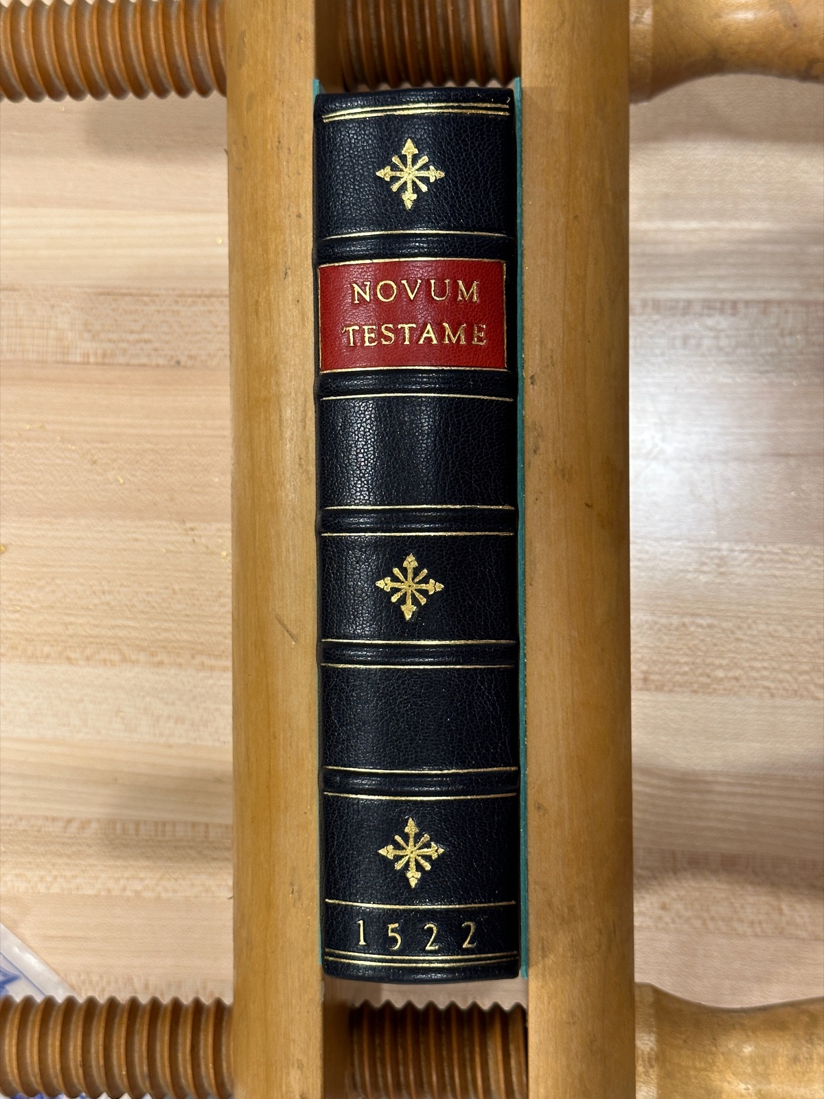 A book in a wooden laying press with the leather spine up, showing the completed gold tooling and hand lettering
