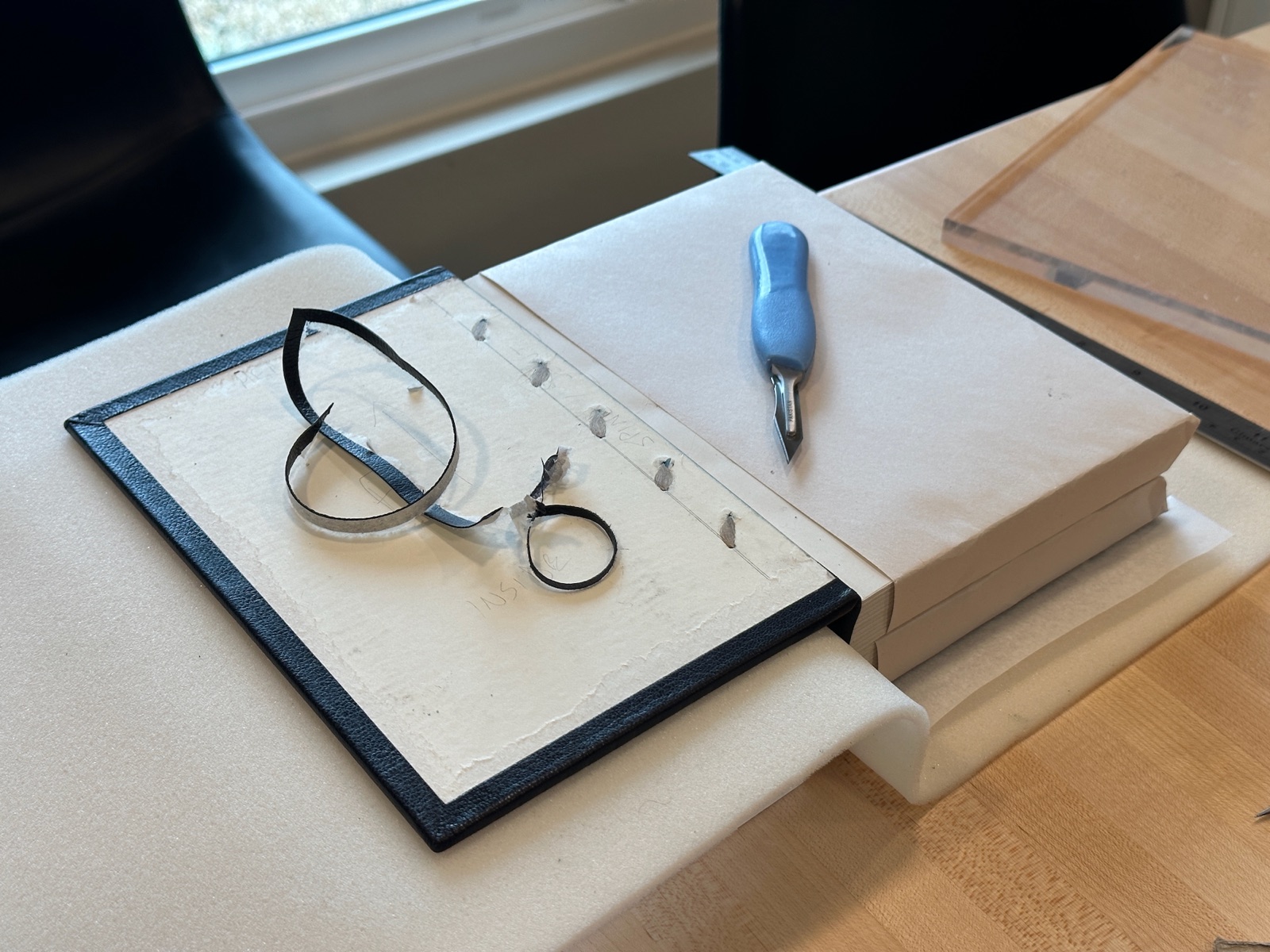 A book opened to the front cover where a scalpel and leather bits are sitting on the cover.