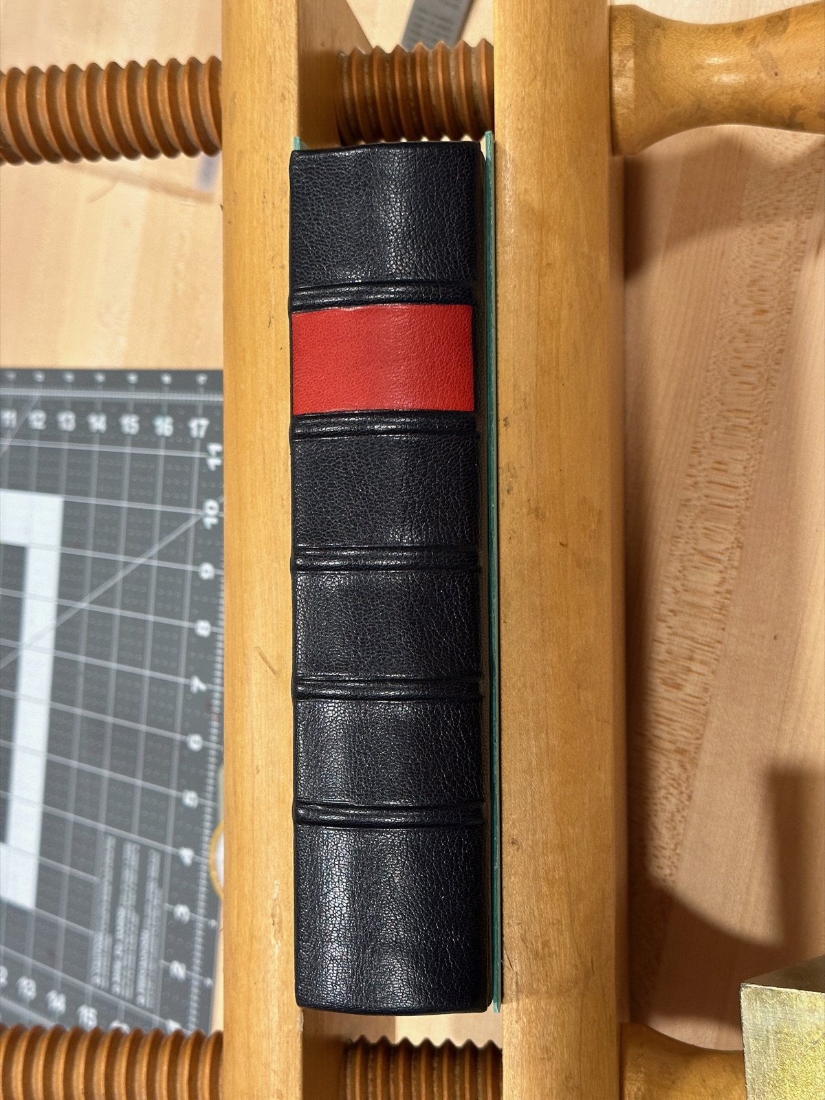 Red leather label on a black leather book inside of a wooden press.