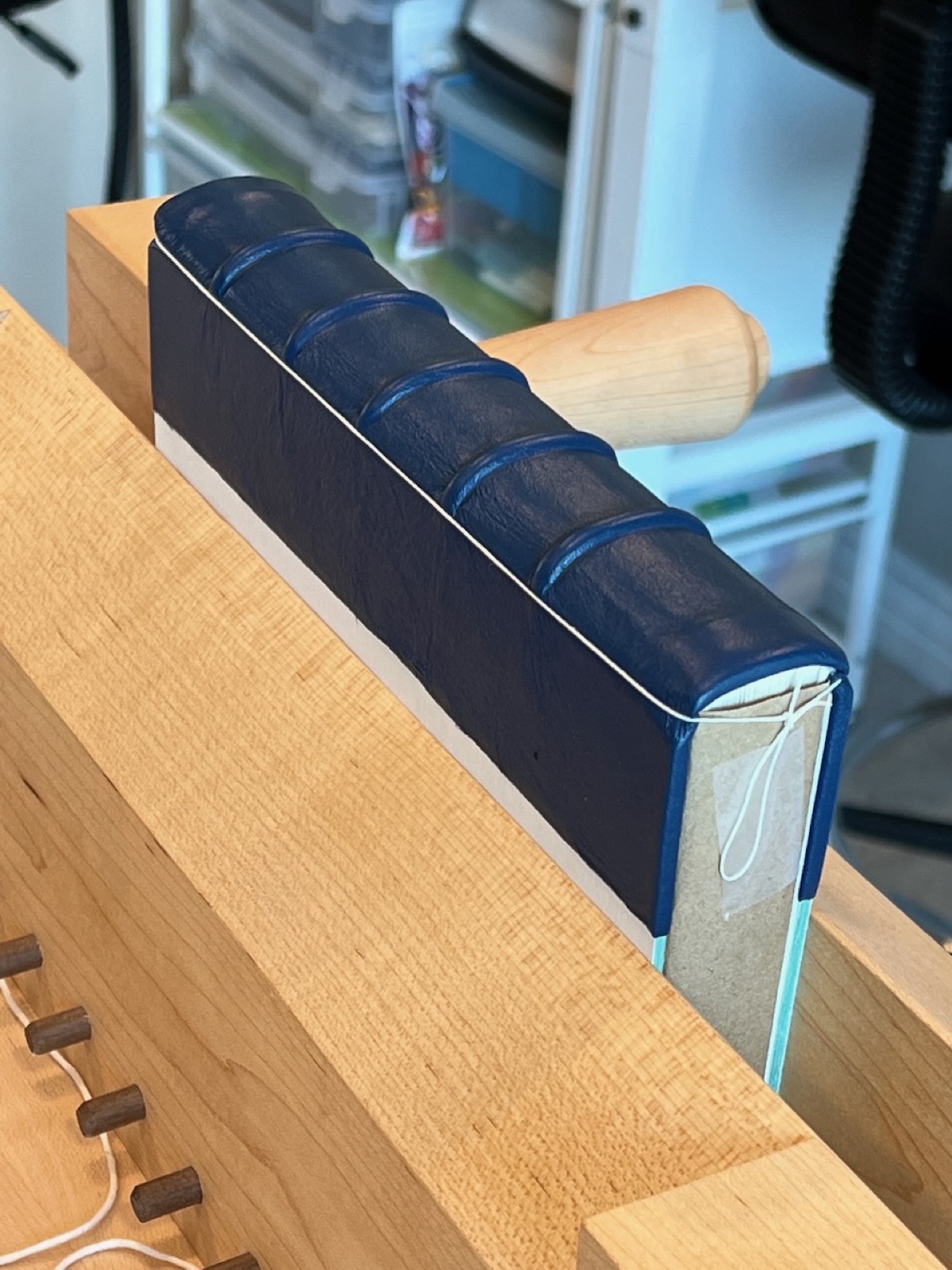 blue leather book in wooden laying press showing the leather over the raised cords.