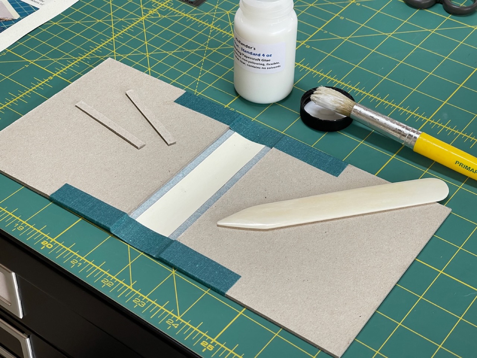 bone folder and adhesives on mat with teal book cover case
