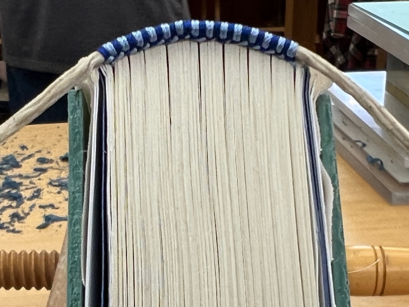 Blue and white silk endbands being sewn onto a text block held in a press.