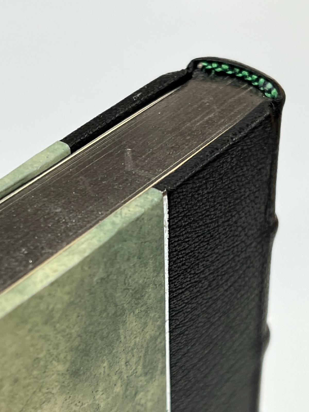 A close up of the top of a book with graphite gilding, black leather, and green decorative paper and green and black end band