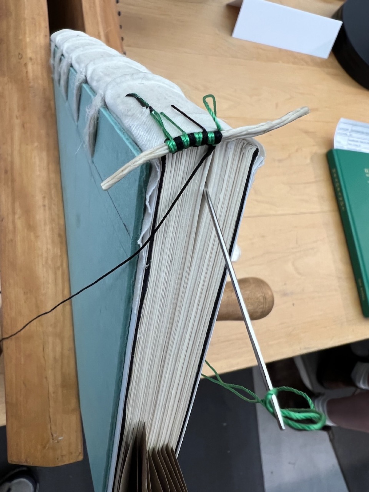 A book in a press with a green and black silk end band half sewn on