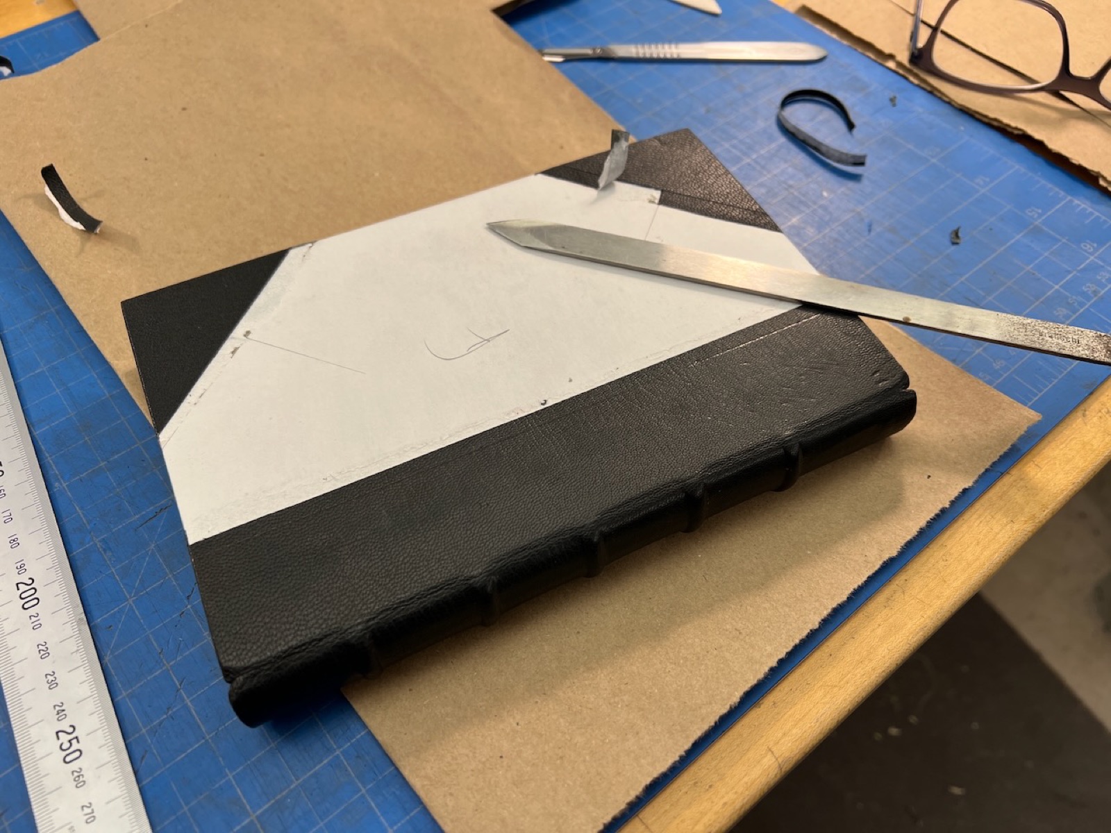 A book lying on the workbench showing black leather spine and corners.