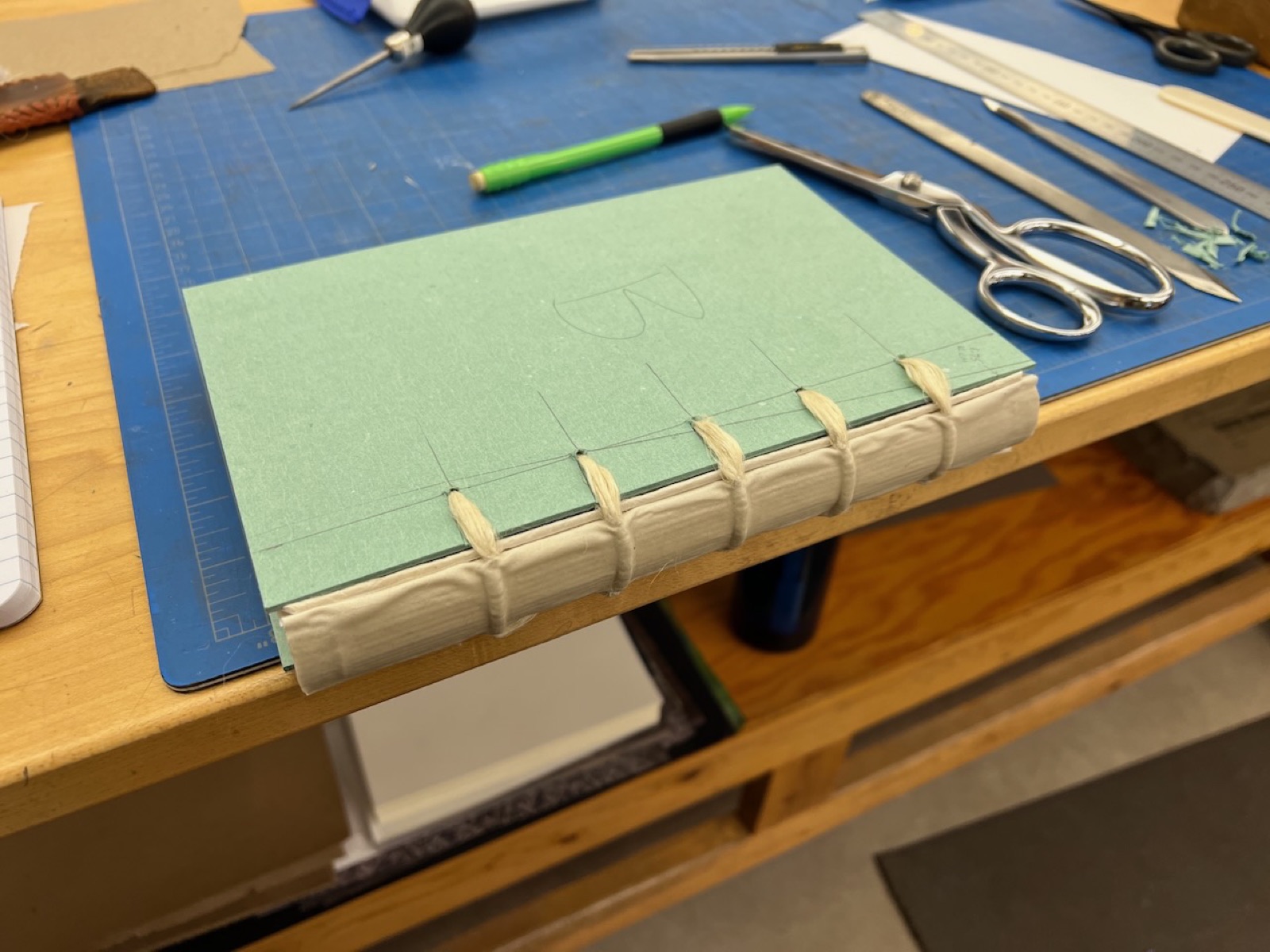 Green cover boards with cords sewn in sitting on a workbench.