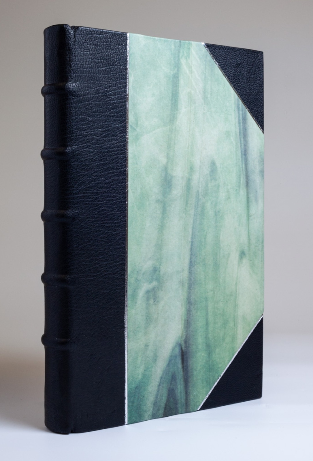 A half-leather binding with black leather spine, raised bands, and green decorated paper sides.