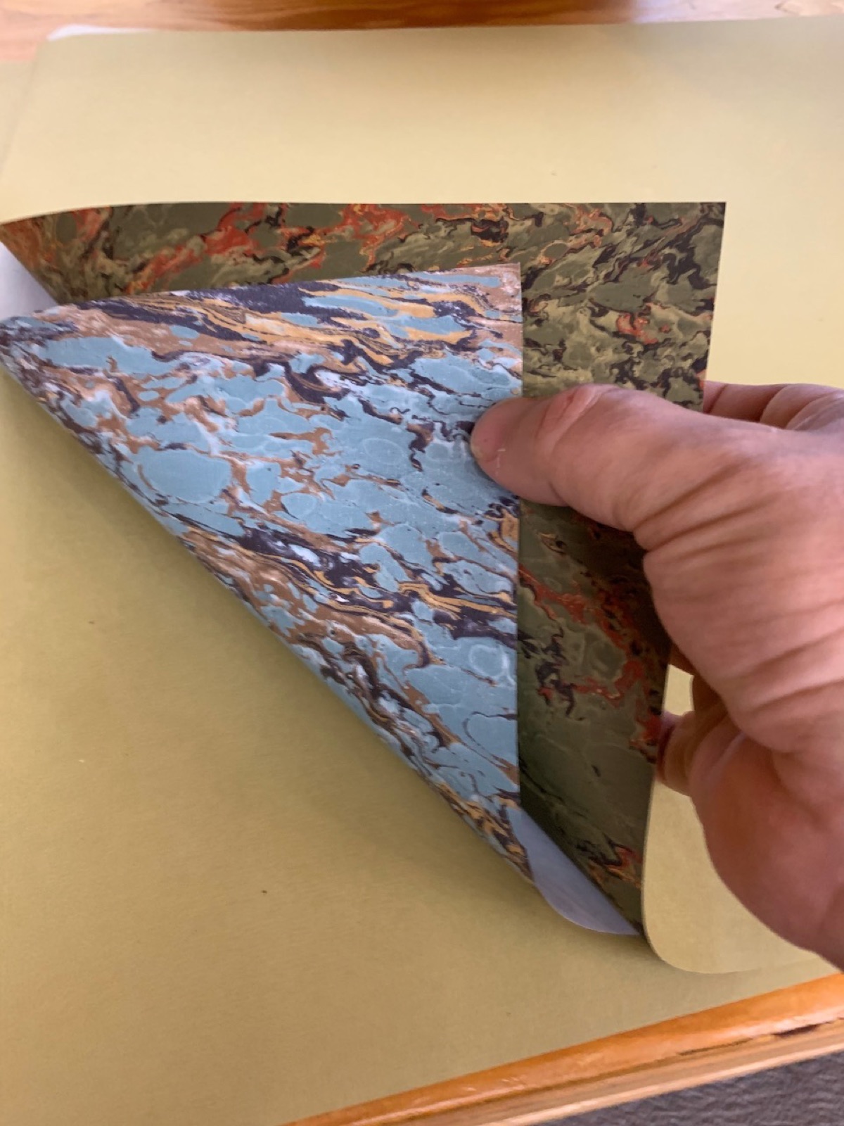 A hand flexing a sheet of marbled paper to feel its grain direction.
