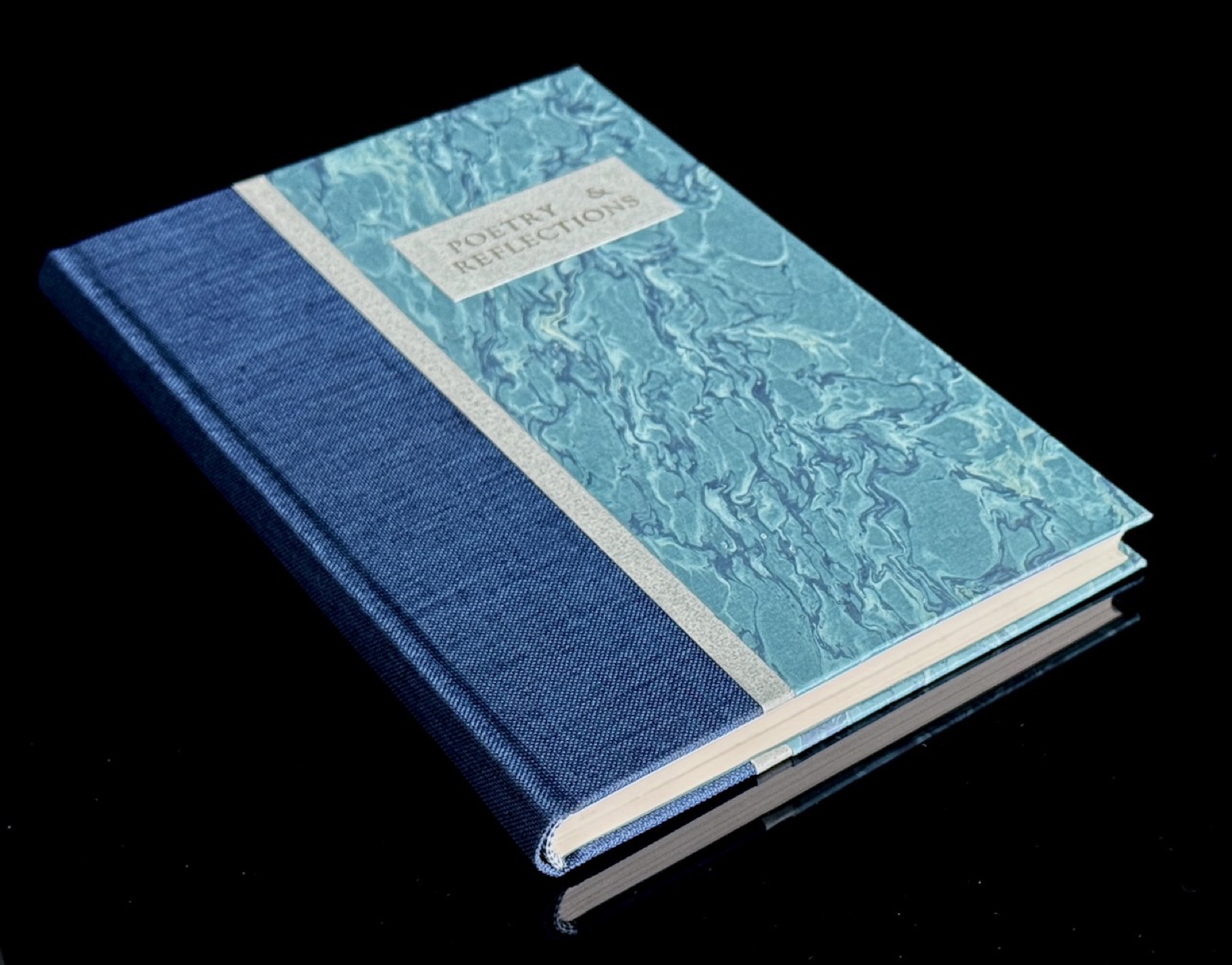 A blue cloth and marbled paper binding titled Poetry & Reflections photographed on black.