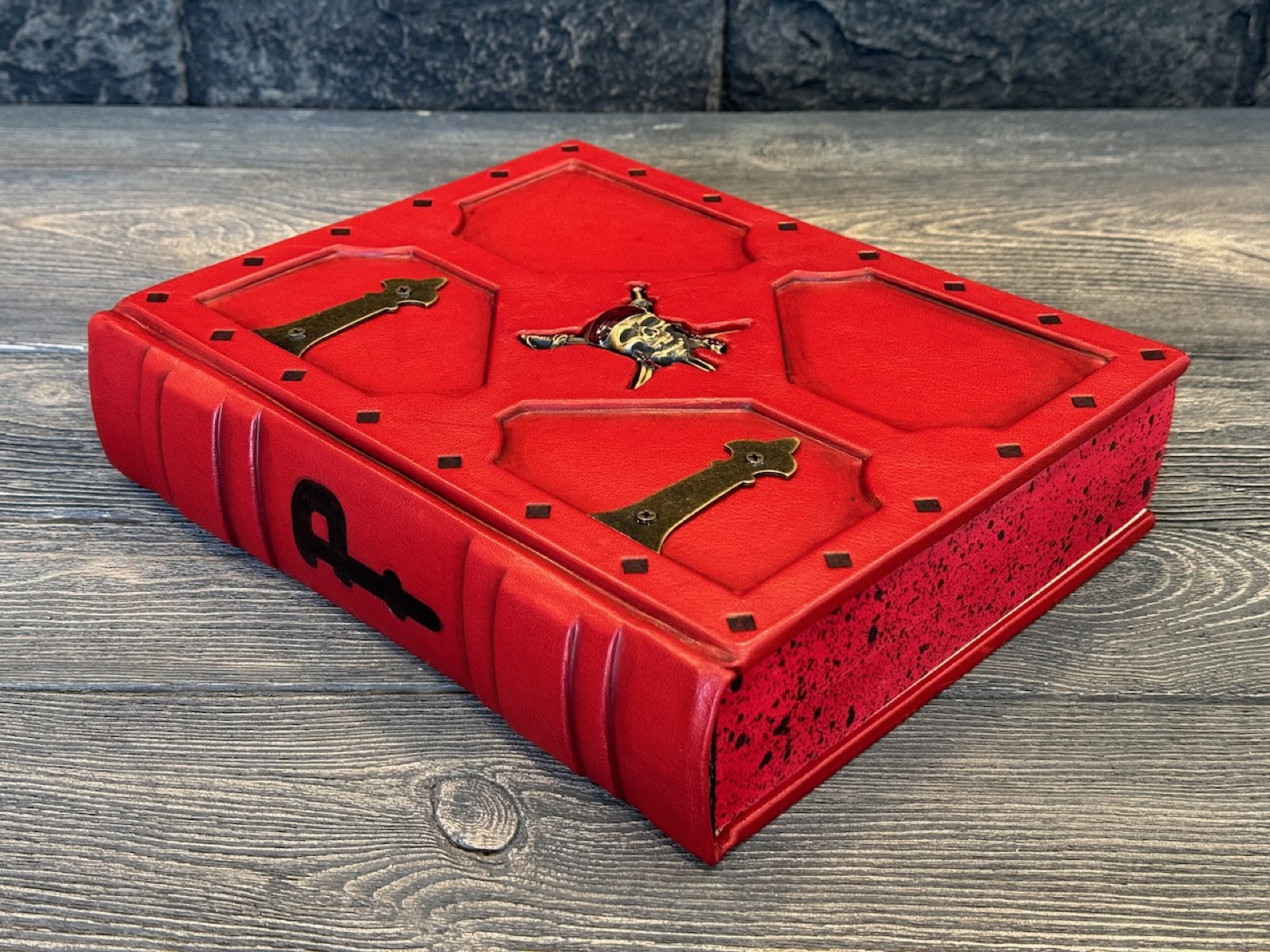 The Pirate Bible: a decorative red leather binding with metal corner and center hardware, on a dark wood surface.