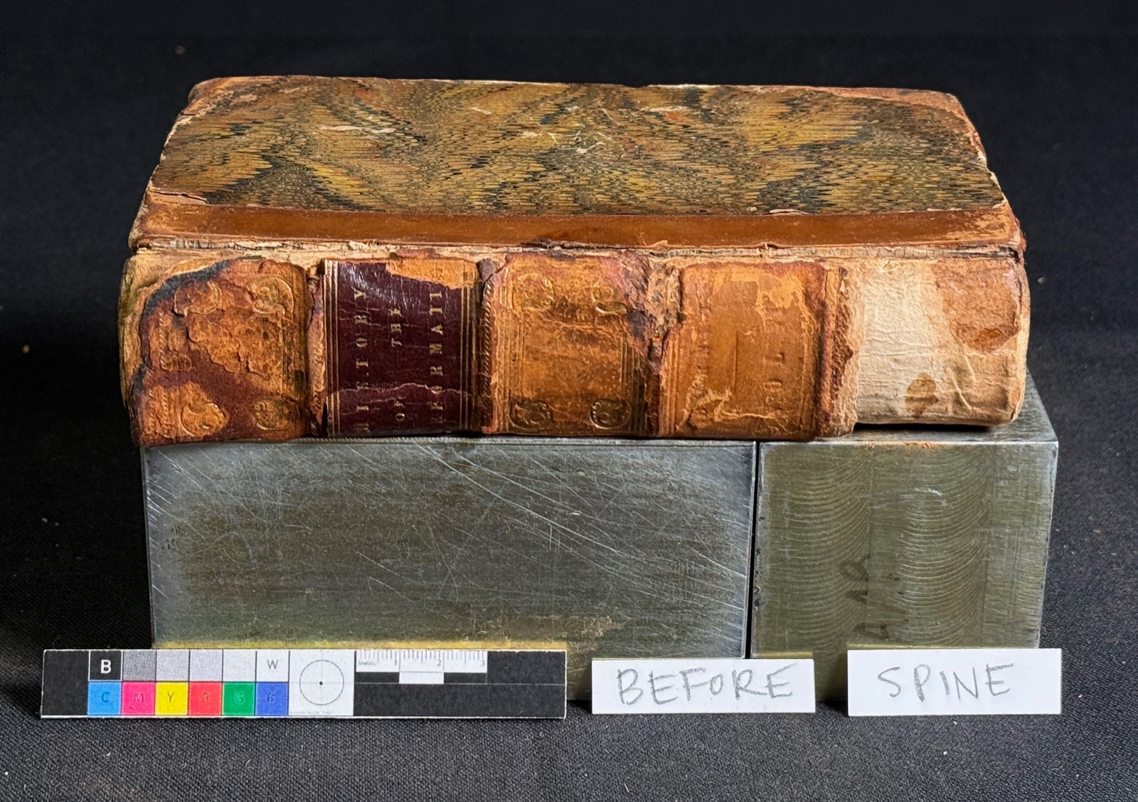 The Reformation volume before treatment: worn leather binding with a damaged, lifting spine and marbled boards, photographed with a color calibration target.