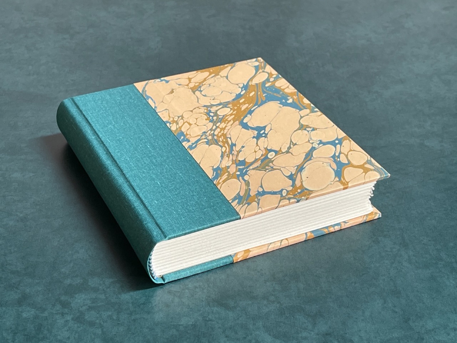 Teal cloth binding with marbled paper sides lying flat.
