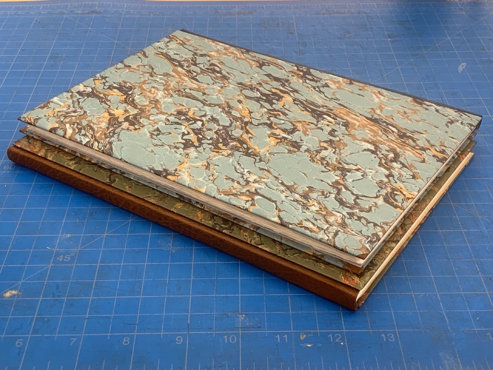 A three-piece binding with leather spine and marbled paper sides on a cutting mat.