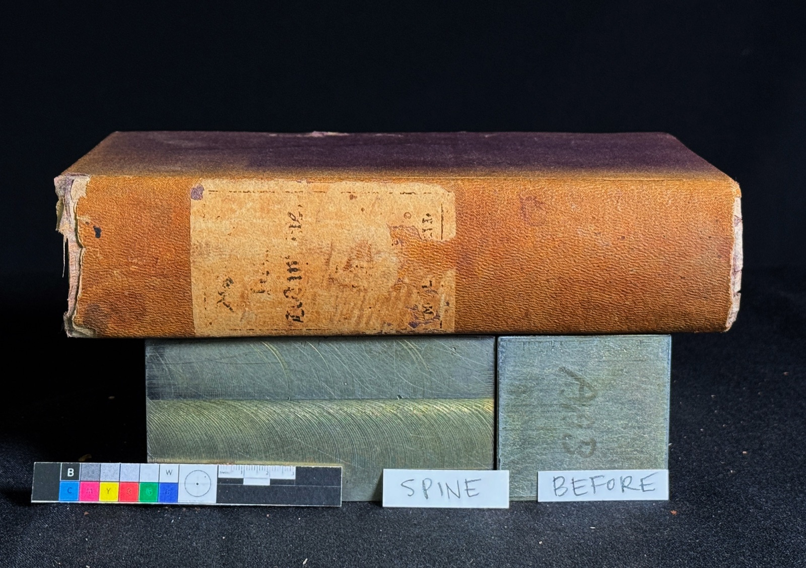 The Tyndale volume before treatment: tan leather binding with a torn, lifting spine, photographed with a color calibration target.