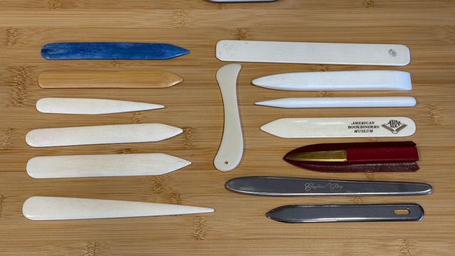 A collection of bone and Teflon folders arranged on a wooden bench.