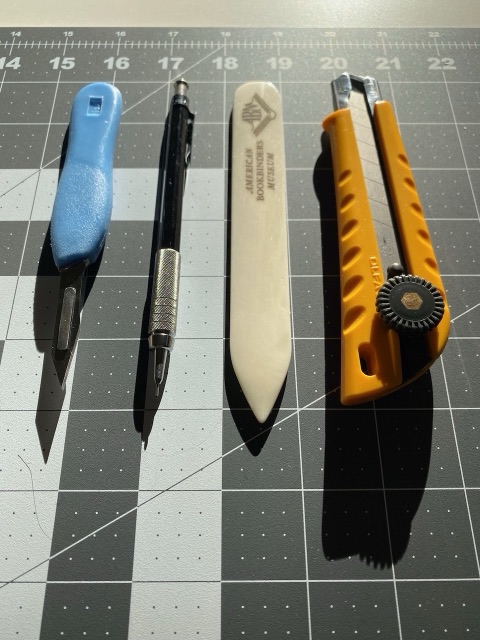 Piercing and cutting tools laid out on a grey cutting mat.