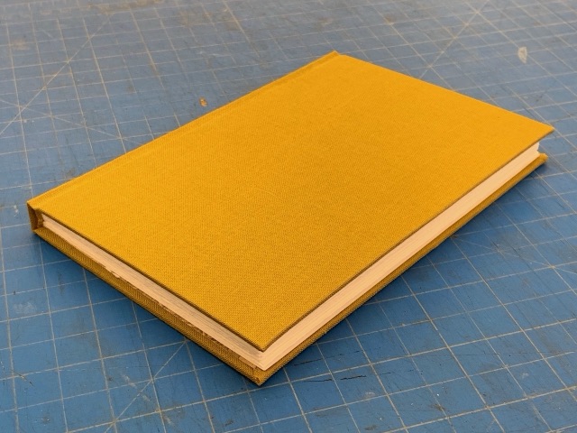 A mustard-yellow cloth-covered flatback notebook lying on a cutting mat.