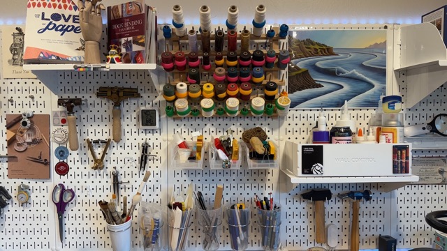 An organized pegboard workshop wall of bookbinding tools and supplies.