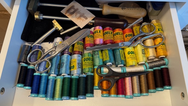 A drawer of colorful linen thread spools with scissors and sewing tools.