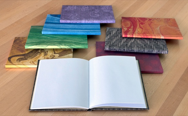 One of the notebooks lying open to blank pages, with more decorative-covered notebooks behind it.