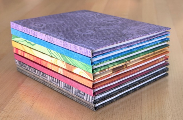 A stack of hardcover notebooks with colorful decorative paper covers.
